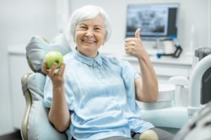 Smiling woman with dental implants in Pasadena holding an apple