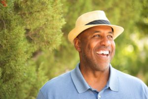 man in blue polo and fedora smiling with dental implants 