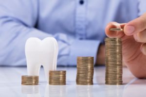 Model tooth next to increasing stacks of coins from dental insurance